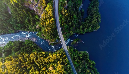 Aerial view of a winding asphalt road crossing a rushing river surrounded by lush autumn forest landscape, travel adventure and nature photography