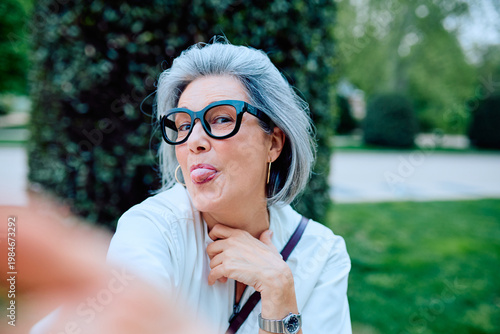 фотографія Senior woman with grey hair and big eyeglasses sticking tongue out, enjoying a f