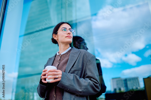 Фотография Businesswoman standing outdoors holding a coffee cup, looking thoughtfully towar