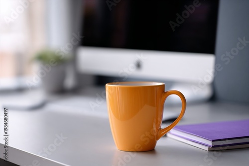 Orange coffee mug on desk with computer in blurred background