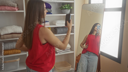 Foto Woman in red top holds smartphone for selfie in dressingroom mirror, posing with arm extended and visible hand; confidence selfcare