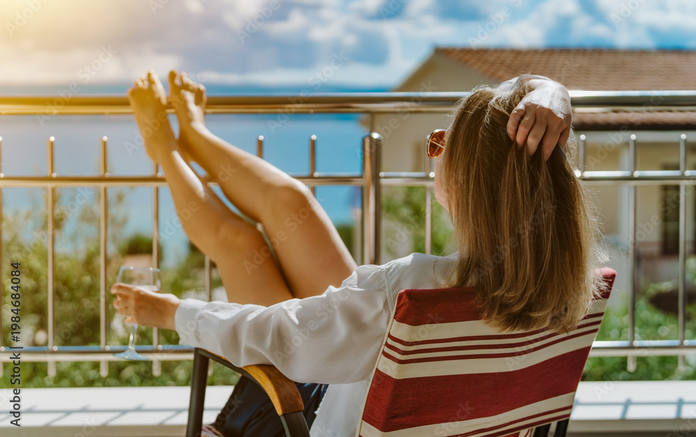 Obraz premium Woman relaxes on sunny terrace with wine.