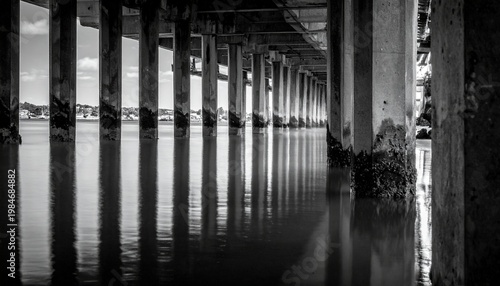 Monochrome view under a pier with reflections in the water.