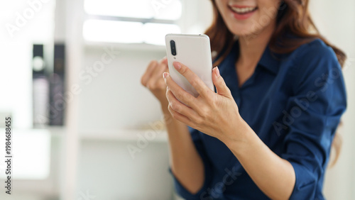 Fotografie Excited Moment: A woman holds a smartphone, her face lit with pure excitement as she reacts to something on the screen