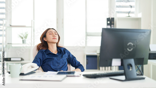 Fotografie Workplace Serenity: A woman finds inner peace, seated serenely in a modern office, basking in the tranquil environment with eyes gently closed