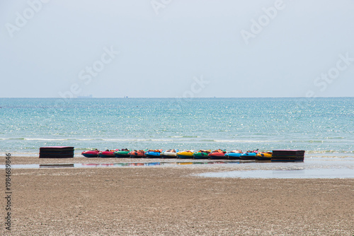 Colorful kayaks are arranged along Toey Ngam Beach for tourists to use on holidays, with the water sea and sky as a backdrop on sunny days.