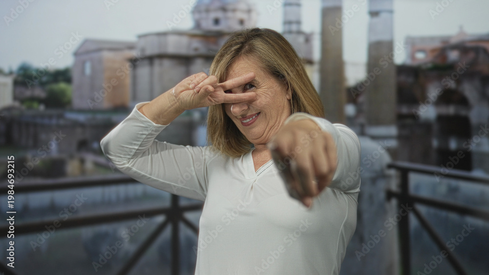 Fototapeta premium Woman in white shirt smiling and pointing finger and making a peace sign at ancient ruins building; playfulness.