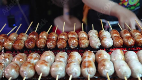 Vendor grilling loads of pork kebabs on grill for locals and tourists outdoors at traditional street food market in Thailand. Person cooking and selling unhealthy snacks, junk food at local bazaar.