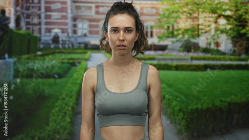 Quadro su tela Hispanic young woman covers mouth with hand for silence outside building as she gazes forward; shock