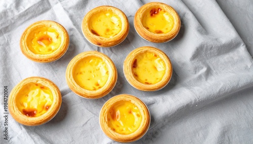 Golden Miniature Egg Custard Tarts with Flaky Pastry Crusts Arranged on a Textured Cloth Surface