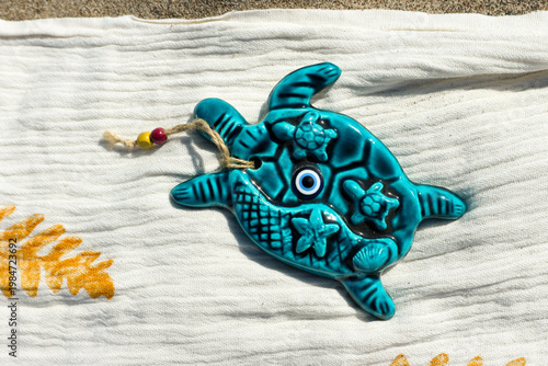Sea turtle figurine with nazar evil eye, a souvenir on a white beach towel at a sandy beach in mediterranean