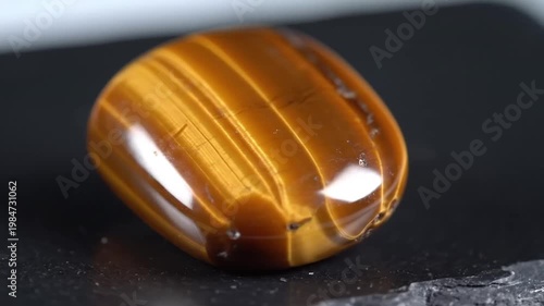 Polished tigers eye gemstone showing golden brown chatoyancy stripes, natural mineral with subtle light reflections on dark textured surface