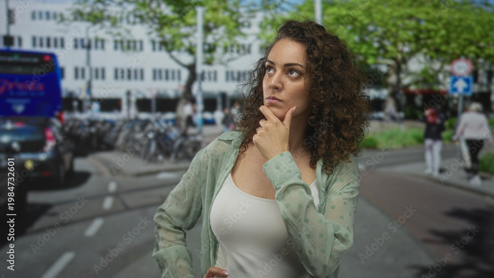 Fototapeta premium Woman showing cleavage looking up with hand on chin on a busy city street among buses and bicycles; contemplation.