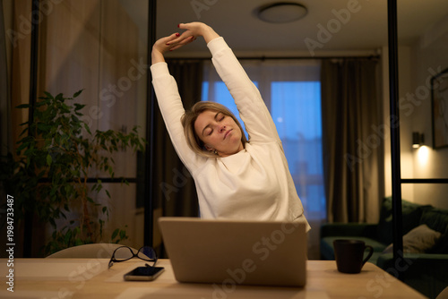 Remote worker taking a long upward stretch at her desk
