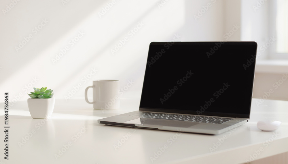 Fototapeta premium A laptop sits on a white desk next to a plant and coffee mug.