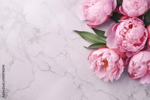 Pink peonies and green leaves decorating a clean white marble surface, offering elegant copy space