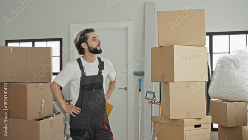 Wallpaper Mural Man with hand on hip surveying stacked cardboard boxes and holding a package in a building; thoughtful moving preparation. Torontodigital.ca