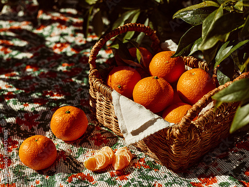 A wicker basket filled with fresh, sun-ripened oranges with green leaves, spilling onto a vibrant floral tablecloth, bathed in warm, dappled sunlight with a vintage film aesthetic.