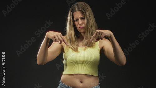 Wallpaper Mural Woman points both index fingers down at navel wearing yellow tanktop in studio; disapproval warning. Torontodigital.ca