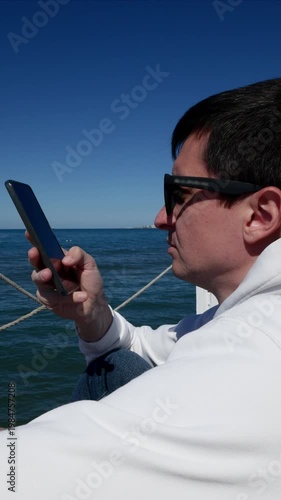 Young man working or scrolling on smartphone, relaxing at the beach.