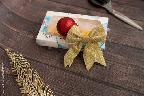 Festive gift box with golden bow and red ornament on wooden surface
