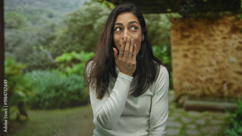 Quadro su tela Woman covering mouth with hand beside a stone building in green countryside; surprise wonder curiosity moment