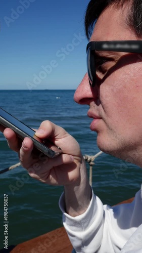 Young man recording voice message at the beach with smartphone, chatting with AI.