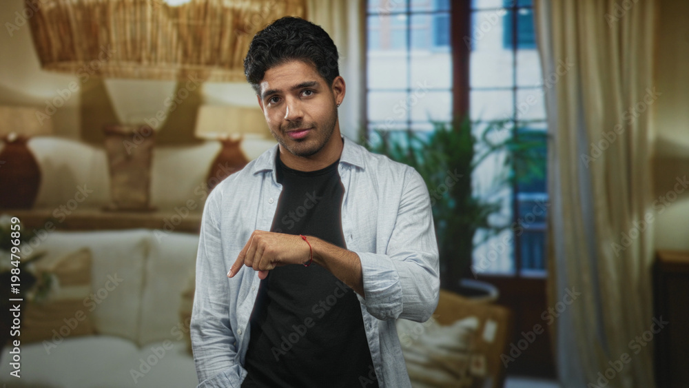 Naklejka premium Smiling man pointing index finger down with right hand toward floor in studio living room set; playful confidence.