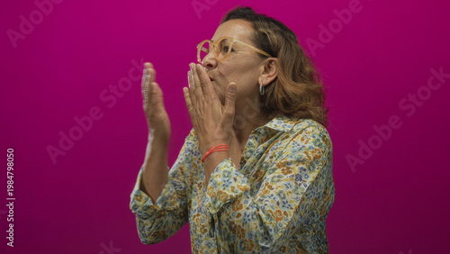 Canvas Print Middle aged hispanic woman with floral blouse and clear glasses blowing kiss in pink studio; affection