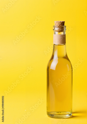 A glass bottle with a cork, filled with oil or apple cider vinegar, on a yellow background for Health Day