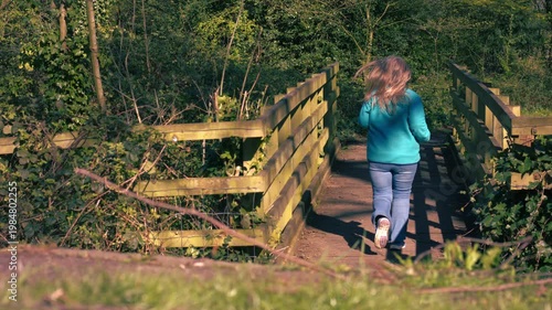 Woman running across wooden bridge woodland in dappled summer sunshine