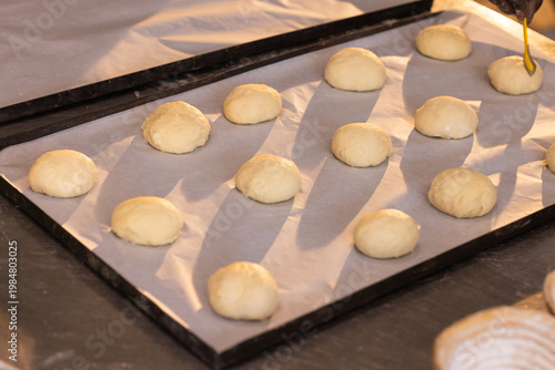 Parchment pan holding raw rolls at bakery counter with yellow brush and floured proofing basket