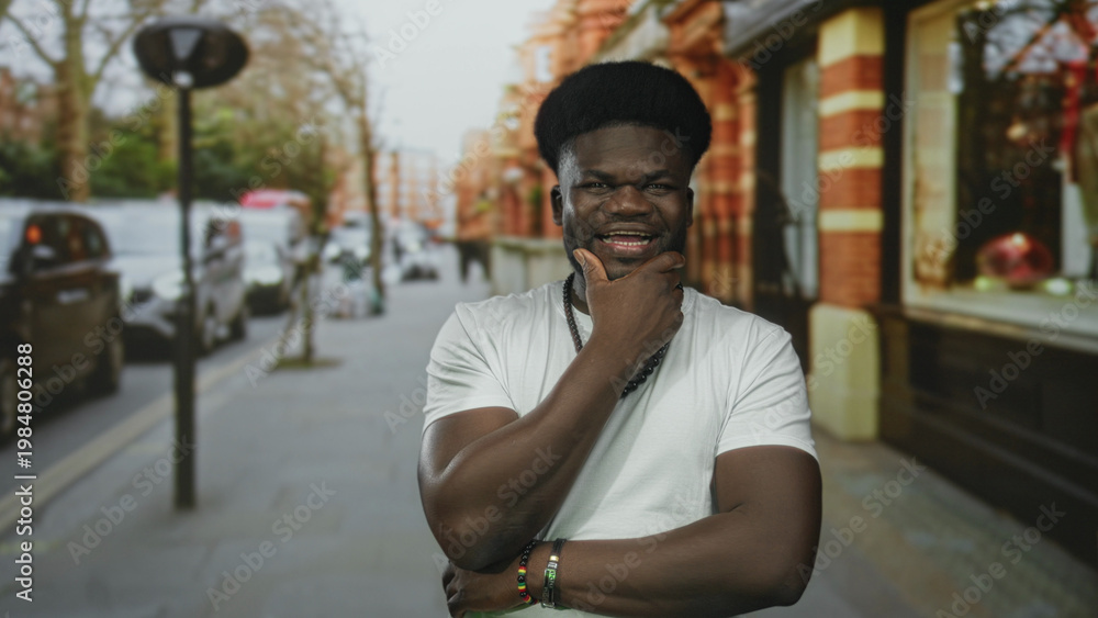 Fototapeta premium Man with hand on chin and open mouth on street near storefront, wearing white t shirt and beaded necklace; playful confidence.