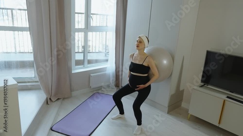 Fitness for pregnant women. Pregnant woman squats with fitball, leaning against wall. Exercises pregnant women in late pregnancy. Back massage with fitball to strengthen back and pelvic floor muscles.