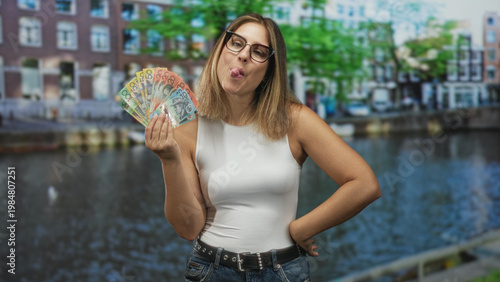 Photography Woman wearing glasses and white tanktop holding australian dollars with hand fanned and tongue out by building; playful confidence