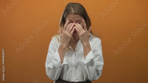 Tableau sur toile Woman pressing hands to eyes rubbing nose bridge in studio with orange wall wearing white shirt; fatigue recovery