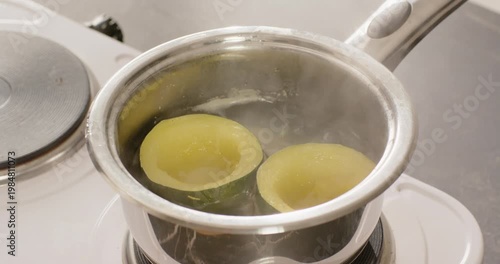 Electric burner is heating water in saucepan, two yellow halves are simmering to soften on cooktop