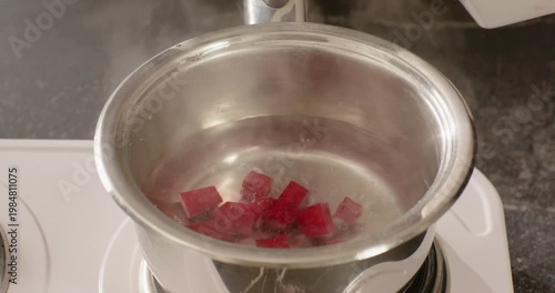 African American hand dropping red cubes into simmering saucepan on stove stirring color into water