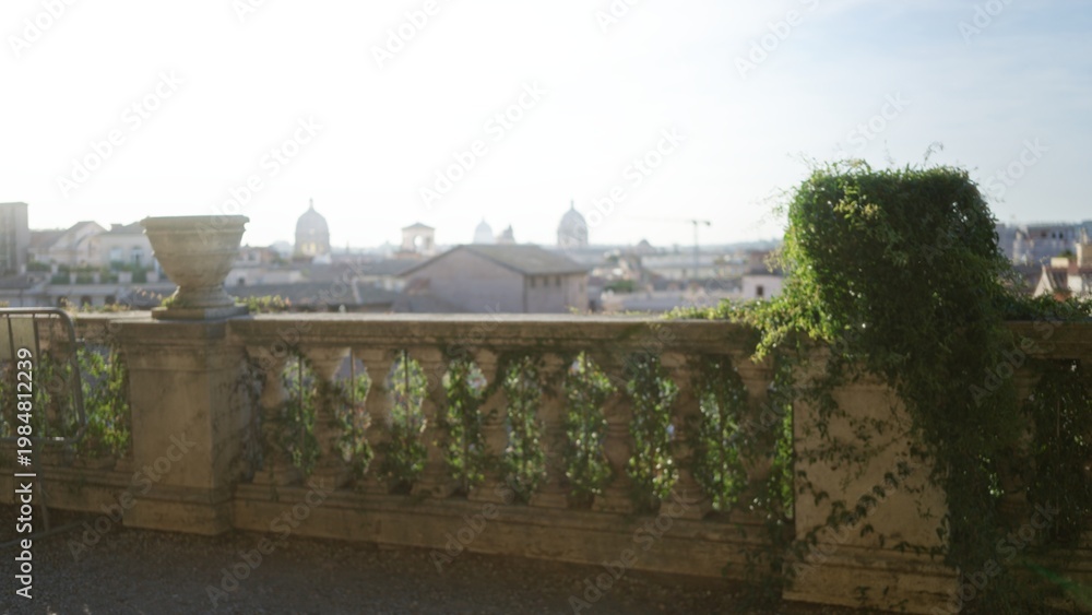 Naklejka premium Sunlit terrace balustrade draped in climbing ivy, distant domes and rooftop softly defocused outdoor; background backdrop copyspace calm.