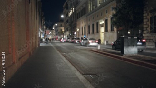 Dimly lit night city street, soft blurred bokeh focus with distant car taillights and building facades; background backplate copyspace.
