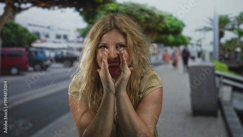 Tableau sur toile Woman cupping hand to mouth shouting on busy city street near parked vans and palm trees with blurred pedestrians; urgent plea
