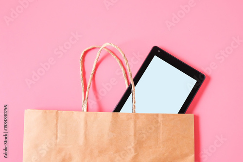Tablet in brown shopping bag on color background.