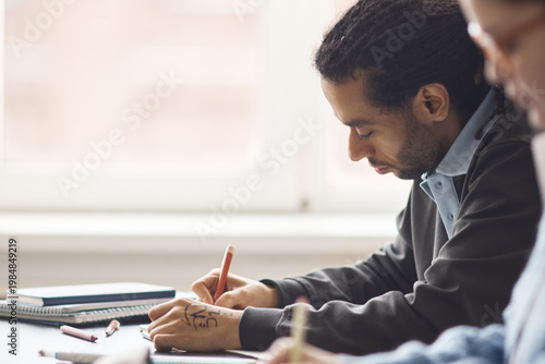 Εκτύπωση καμβά Multiethnic young adult man writing notes during classroom session, showing focus, learning, academic engagement