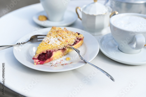 Cheesecake with cherries and crumble topping, a coffee cup and a vintage sugar bowl on a white table, a typical European afternoon dessert, copy space, selected focus,