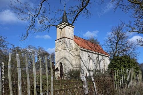 Jager Church Chapel, a small Protestant village chapel built in 1830 surrounded by a rusty iron fence and sections of wooden picket fencing, near Greifswald, Germany