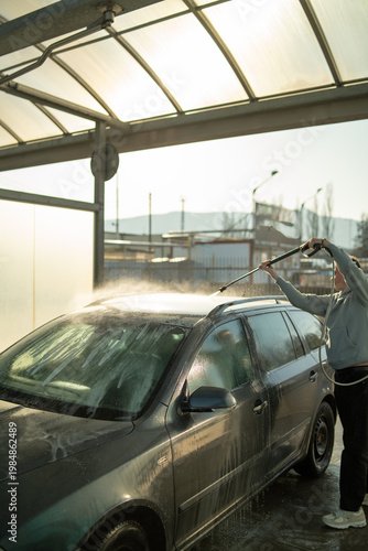 Man rinsing car with water at self service car wash during sunset in Czech Republic Europe. Vehicle cleaning and transport maintenance concept for commercial use.