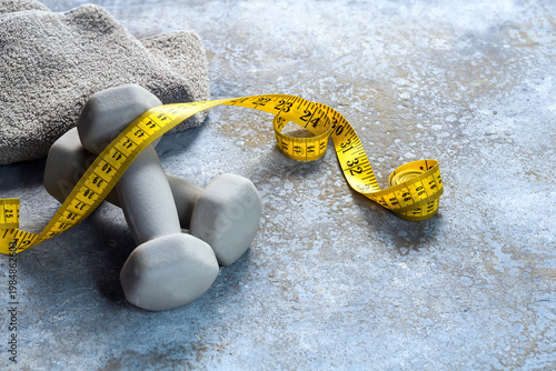 Gray-blue dumbbells and a yellow tape measure on rough stone, concept for fitness and health through exercise and strength training, copy space