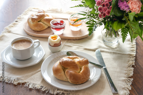 Breakfast with soft bread rolls, jam, boiled eggs, and coffee on a table with a bouquet of flowers, for Easter, Weekend or Mother's Day, selected focus