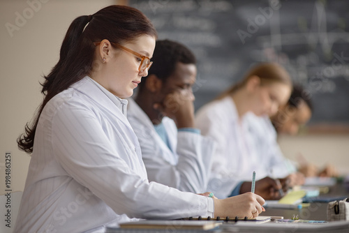 Φωτογραφία Young adult woman writing test while studying next to multiethnic medical students during classroom training
