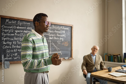 Quadro em tela Young Black man presenting economics lesson beside chalkboard while senior male